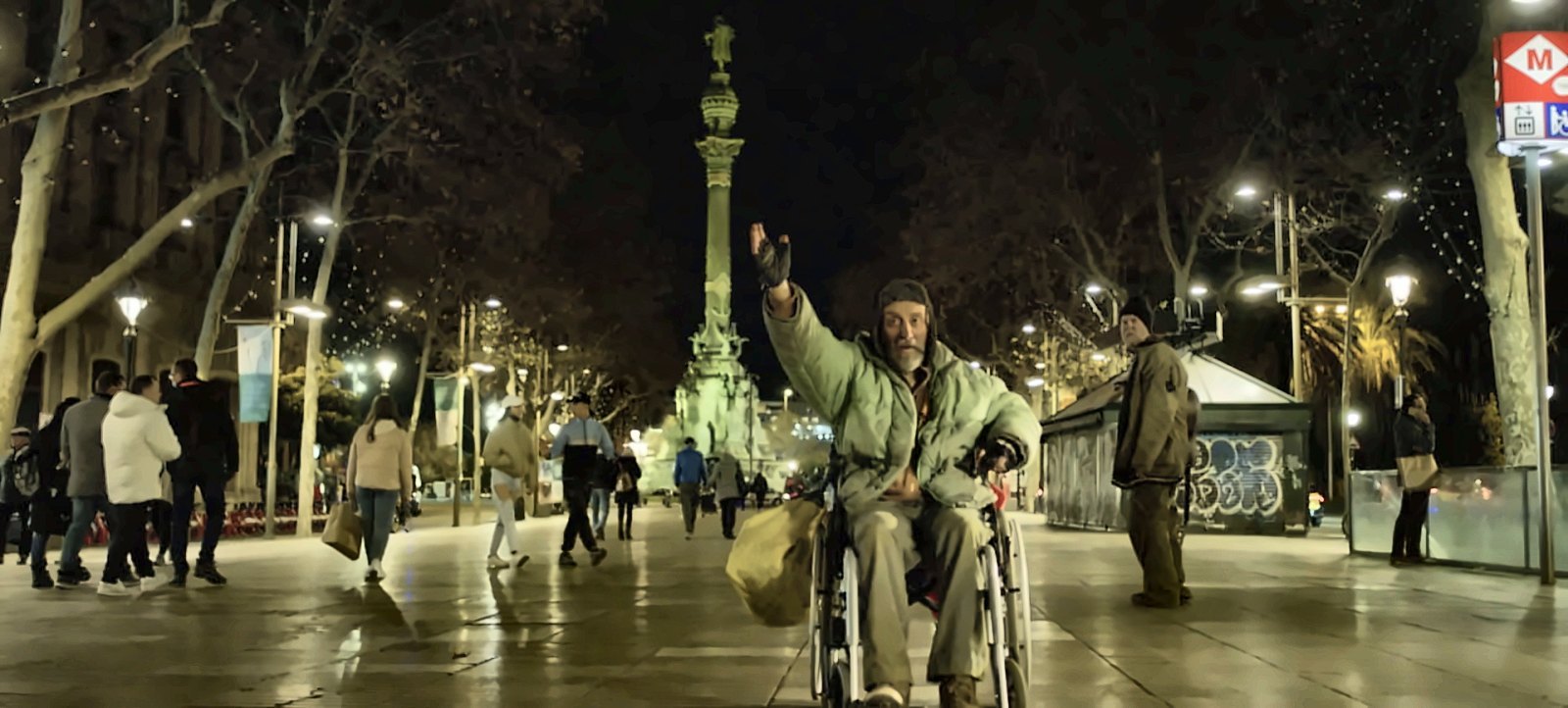 Olli ja pyörätuolissa istuva Lluc yöllä Ramblan päässä Kolumbuksen patsaan edessä. Kohtaus elokuvasta Don Quijote Barcelonassa.