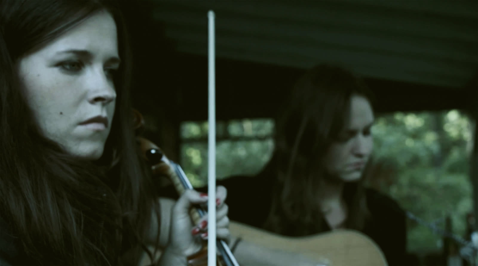 Jemina and Selina Sillanpää singing on a porch. Still from the music video Kahteen suuntaan.